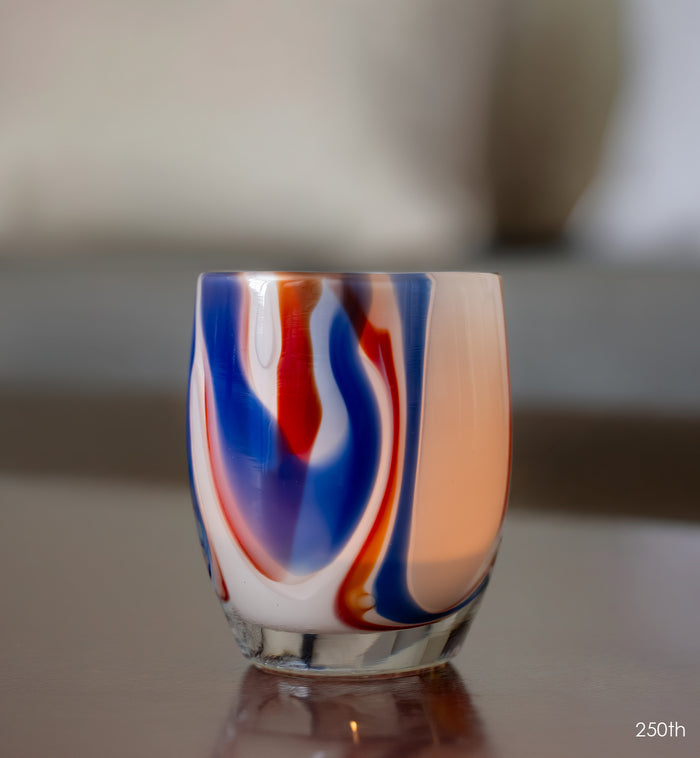 Colorful glass candle holder with red, blue, and white swirls on a reflective surface.