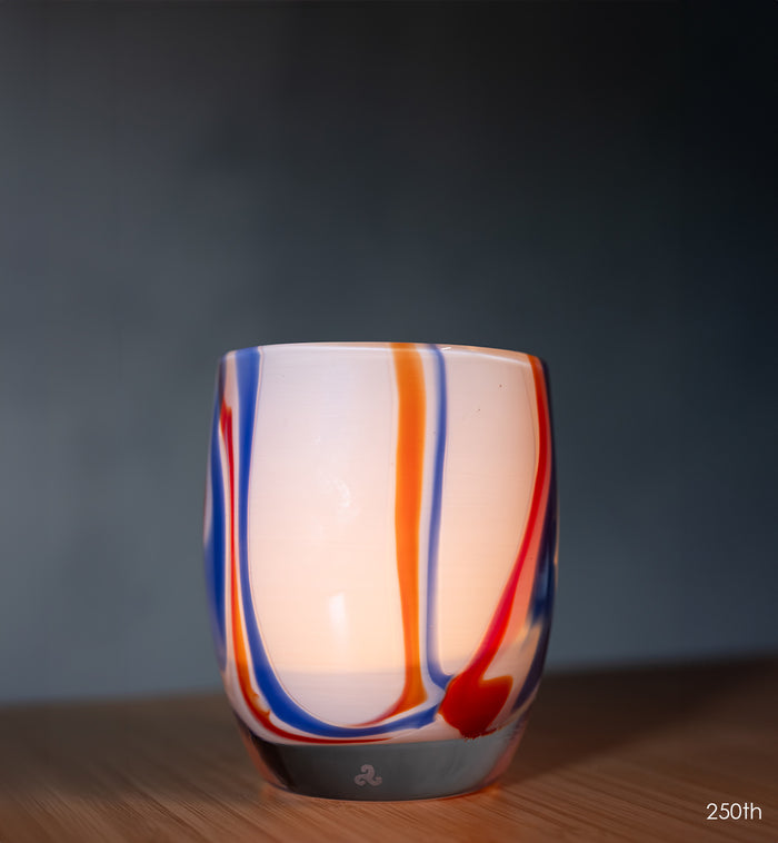 Glass candle holder with colorful swirls on a wooden surface and dark background