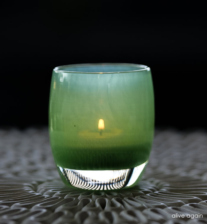 A vibrant green glass candle holder with a candle lit inside, on a patterned surface.