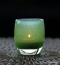 A vibrant green glass candle holder with a candle lit inside, on a patterned surface.