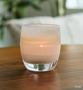 angel light yellow, hand-blown glass votive candle holder on a wood table with cushion and plant blurred in background.