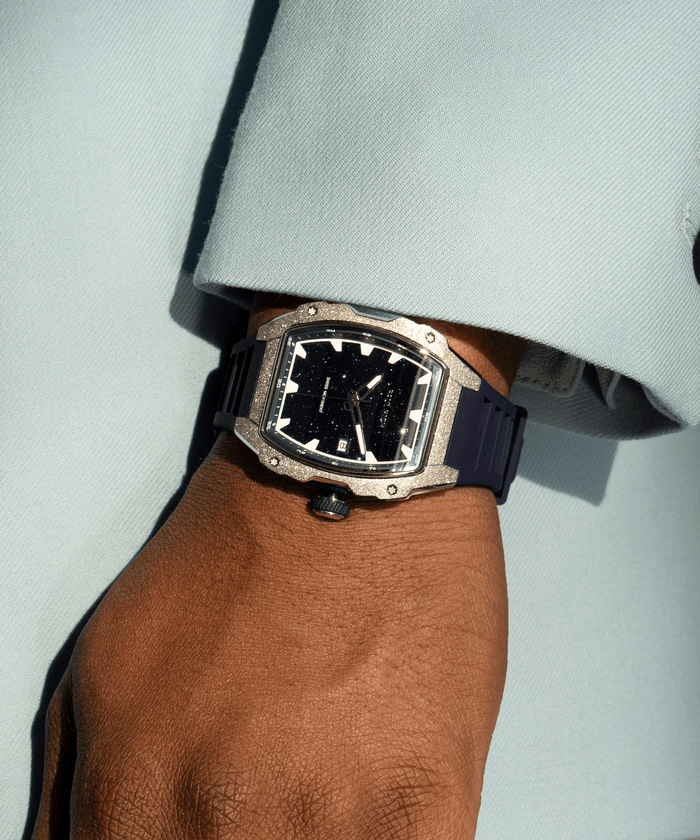 Paul Rich watch with tonneau case, frosted silver bezel, and blue aventurine dial, worn on wrist with light blue sleeve in sunlight.