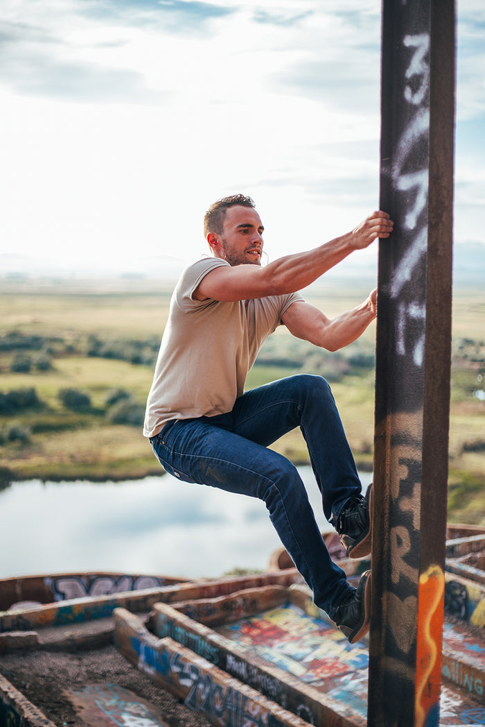 Lifestyle image of man climbing metal beam wearing Bandido Earbud. His muscles are poppin'