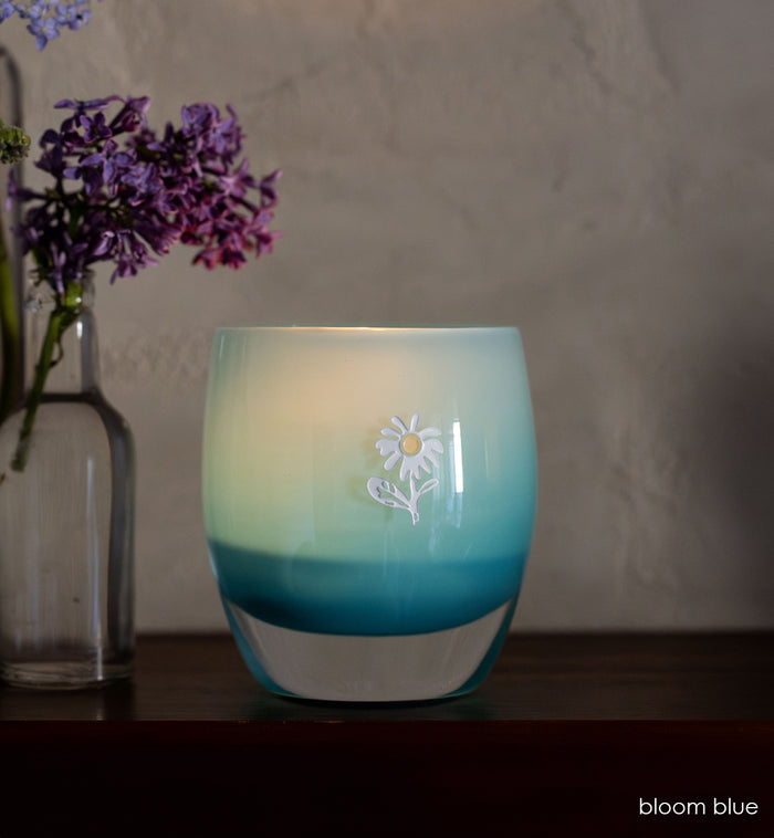 bloom blue glassybaby with white flower etched on it sitting on wood shelf.