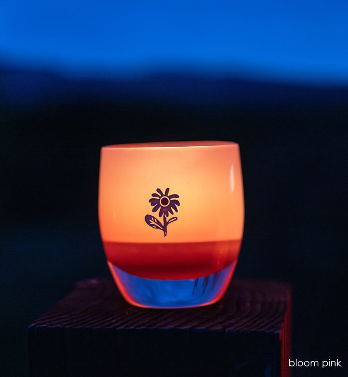 bloom pink glassybaby with white flower etched on sitting on wood shelf at night