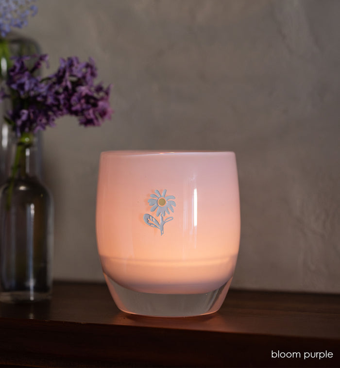 bloom purple glassybaby with white flower etched on it sitting on wood shelf.