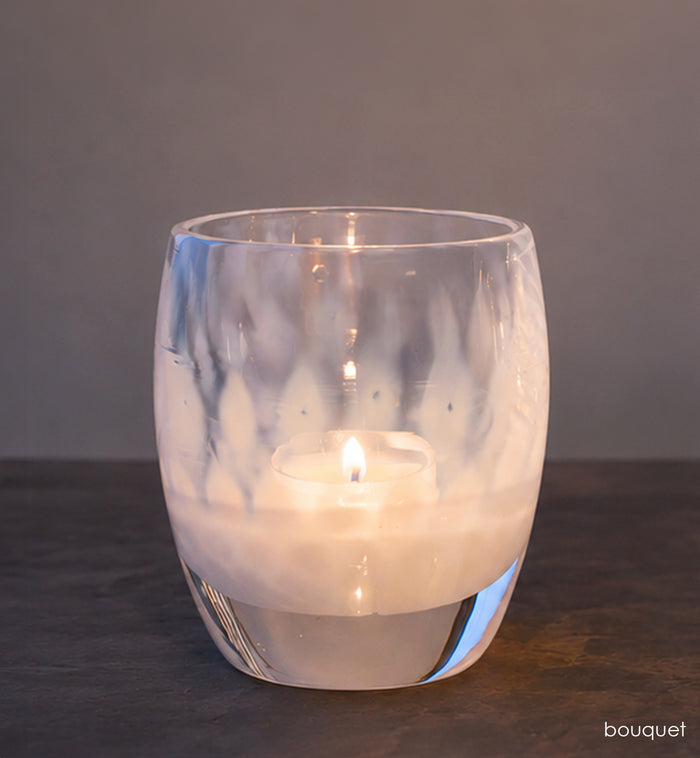 Clear glass candle holder with a lit candle on a dark surface and gray background