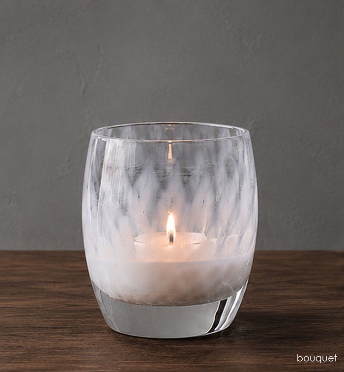 Glass candle holder with a candle on a wooden surface and gray background