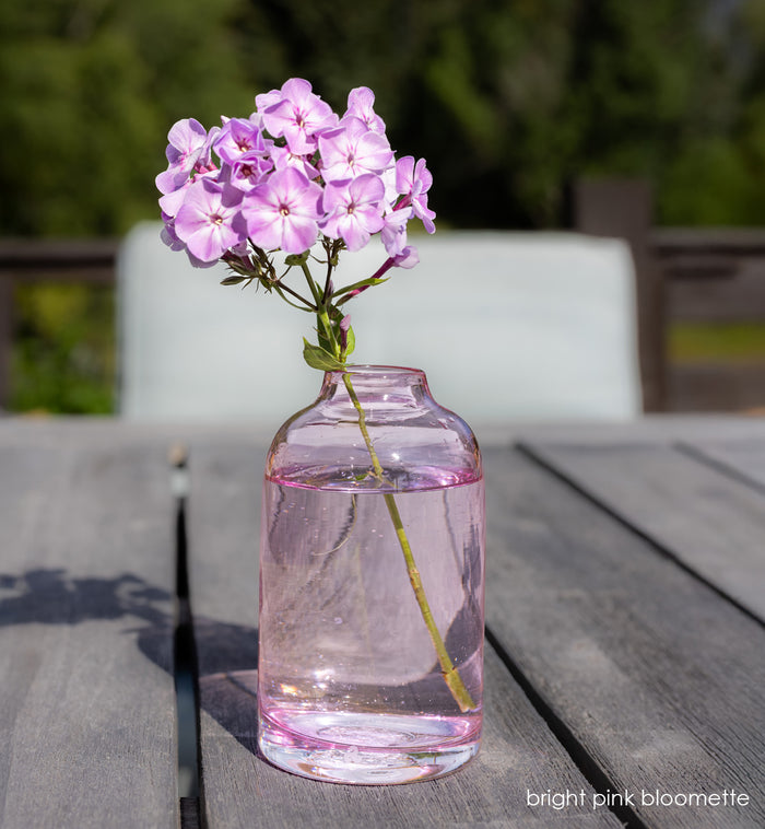 bright pink bloomette - pink vase with pink flower on wood table outside.