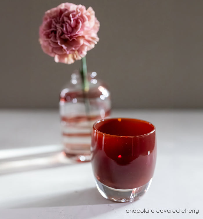 chocolate covered cherry, red brown hand-blown glass votive candle holder with red ribbon bloomette in the background.