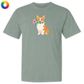 A sage green short-sleeve t-shirt with a graphic of a corgi holding a flower crown on the chest, displayed on a solid white background with a color wheel icon in the top-left corner.