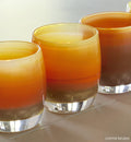 three creme brûlée caramel, hand-blown glass votive candle holders in a row on a tiled surface.