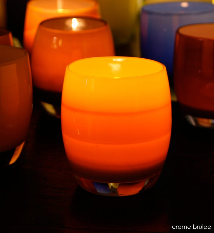 creme brûlée caramel, hand-blown glass votive candle holder lit in a dark room with peace.