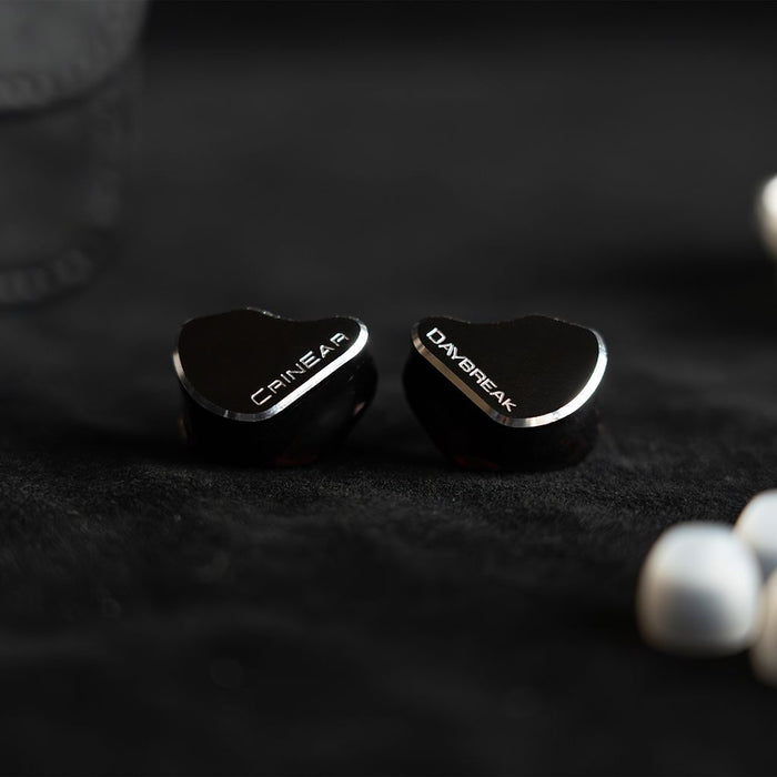 A pair of Crinear Daybreak In-Ear Headphones by Crinear with white ear tips rest on a dark surface, offering audiophile-grade sound as highlighted on headphones.com.
