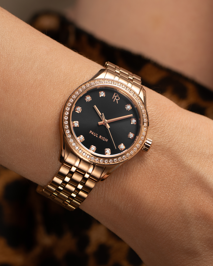 Paul Rich rose gold women’s watch with crystal hour markers and black dial, shown on wrist against leopard print background.