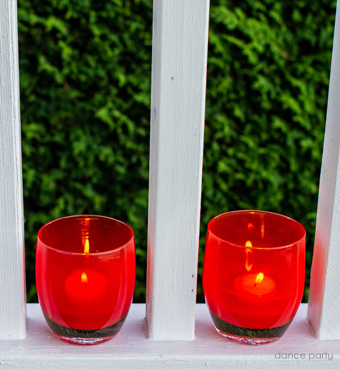 dance party ginger red, hand-blown glass votive candle holder placed between white rails on the porch.