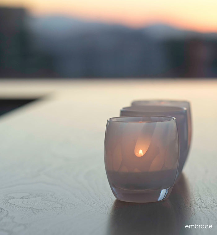 two embrace white with petal, hand-blown glass votive candle holders on a table overlooking the sunset.