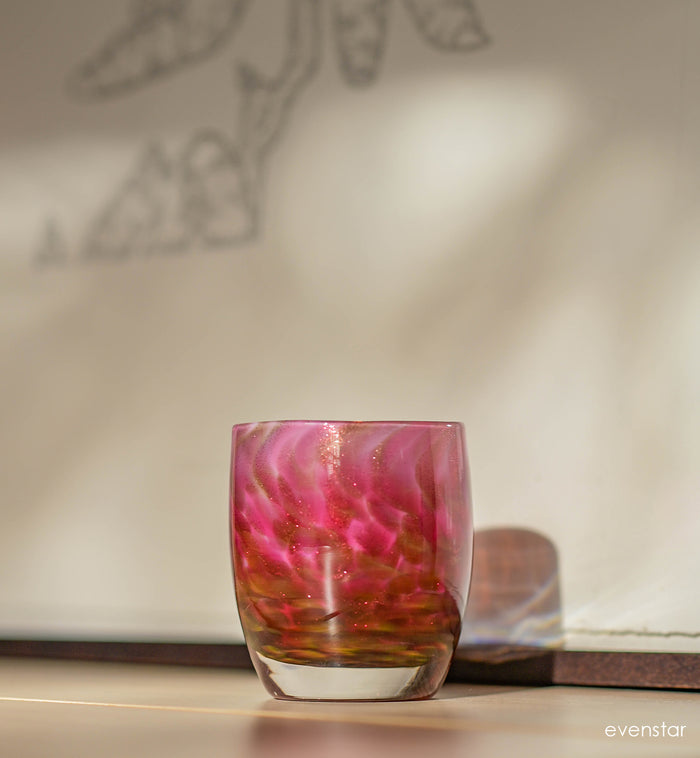 evenstar pink and gold glitter hand-blown glass votive candle holder on a mantle with cream and black line art in the background.