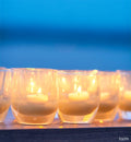 several faith translucent cream hand-blown glass votive candle holders lit at dusk on a wood table.