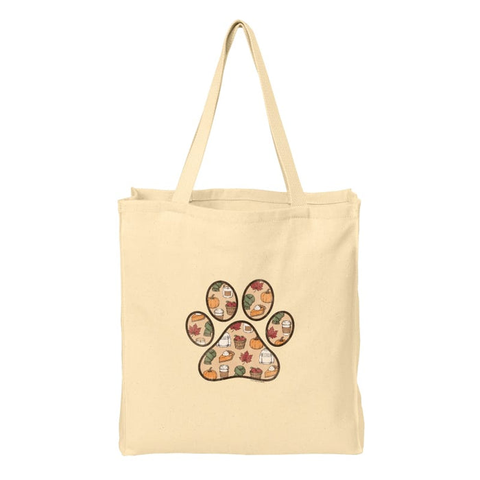 A natural canvas tote bag with a large paw print graphic on the front, filled with a colorful autumn-themed pattern of pumpkins, leaves, and fall foods, shown against a plain white background.