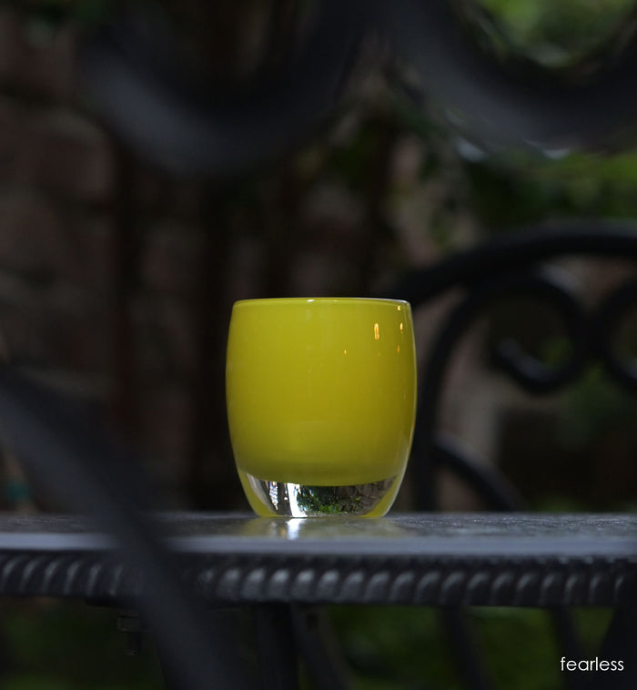 fearless bright yellow hand-blown glass votive candle holder on dark outside table.