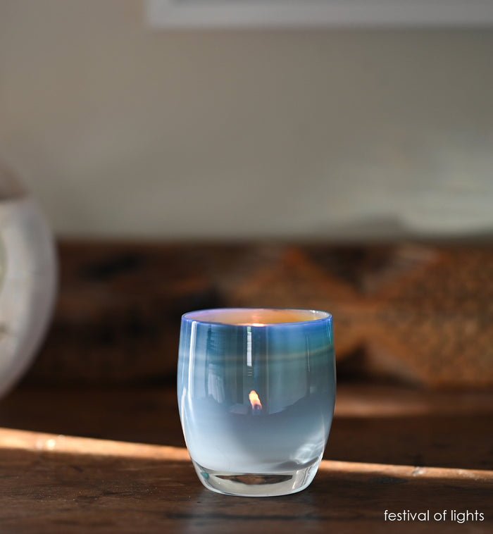festival of lights blue white, hand-blown glass votive candle holder on a wood table with wood bench blurred in background.