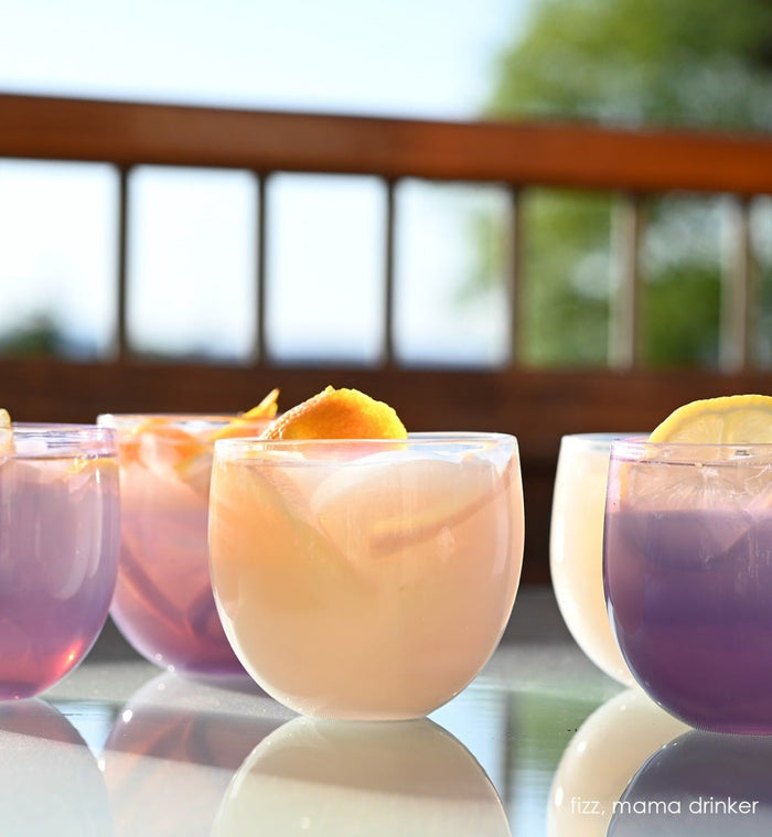 fizz drinkers, white hand-blown drinking glasses with mama drinkers on a sun deck, all filled with liquid and orange peel.