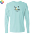 A light aqua long-sleeve t-shirt with a cartoon graphic of a dog in a boat with seagulls flying above, and the text 'flock off' printed below. A small multicolor color wheel icon is visible in the top-left corner.