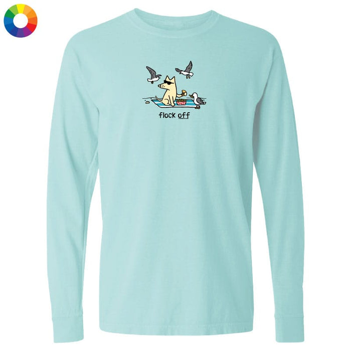 A light aqua long-sleeve t-shirt with a cartoon graphic of a dog in a boat with seagulls flying above, and the text 'flock off' printed below. A small multicolor color wheel icon is visible in the top-left corner.