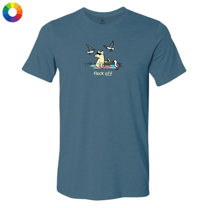A slate blue crewneck t-shirt featuring a cartoon graphic of a dog sitting on a blanket with seagulls flying around, and the text 'flock off' printed below. A small circular color wheel icon is visible in the top-left corner.