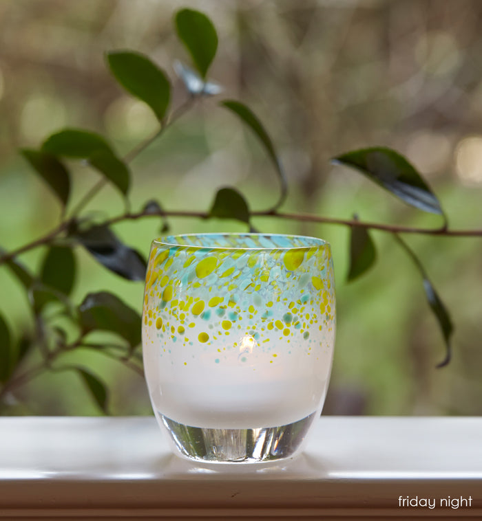 friday night blue green topped hand-blown glass votive candle holder, on a windowsill looking over a green yard.