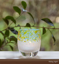 friday night blue green topped hand-blown glass votive candle holder, on a windowsill looking over a green yard.