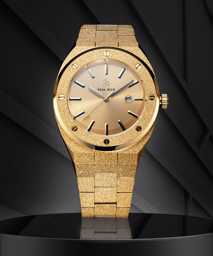 Paul Rich watch with frosted gold case and bracelet, metallic champagne gold sunray dial, and date window, displayed on a black geometric background.