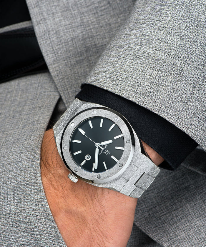 Paul Rich watch with frosted silver case and bracelet, metallic black sunray dial, and date window, worn on wrist with grey suit and black cuff.