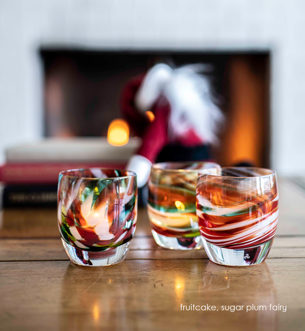 fruitcake, multicolored petal texture, hand-blown glass votive candle holders with sugar plum fairy on a wood table with books and a decorative santa blurred in the background.