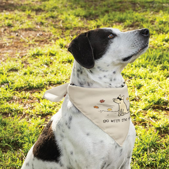 A black and white spotted dog wearing a beige bandana with a cartoon dog graphic and the text 'go with the f.