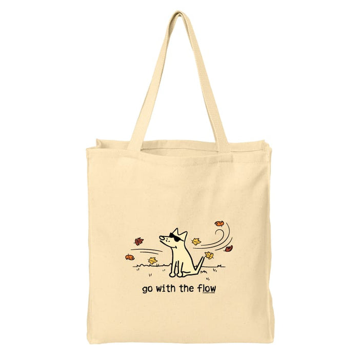 A natural beige canvas tote bag with two shoulder straps, featuring a minimalist black line art illustration of a dog surrounded by autumn leaves and the text 'go with the flow' printed on the front.