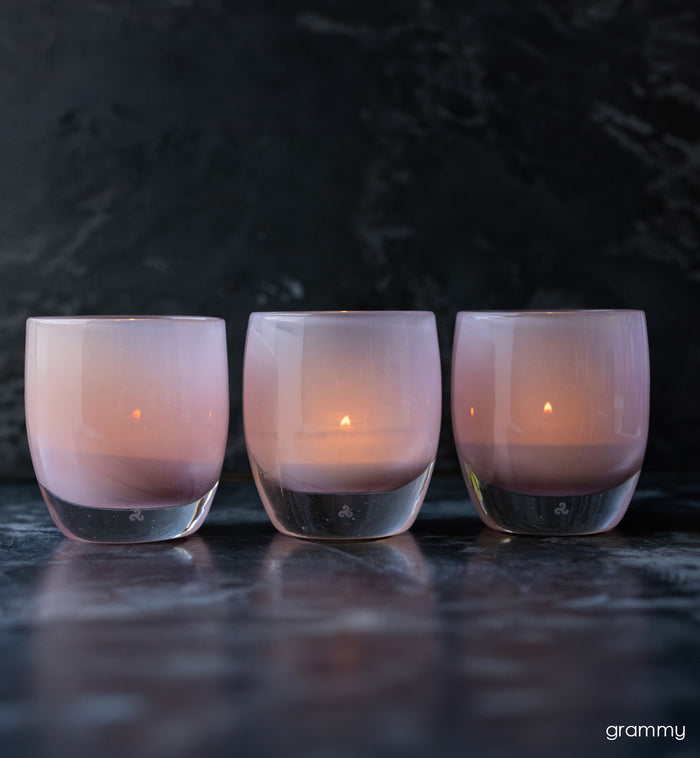 group of grammy, soft pink hand-blown glass votive candle holders on black backdrop.