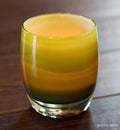 granny smith, striped green with a stark white interior, hand-blown glass votive candle holder glowing with a lit tealight inside on a wood surface.