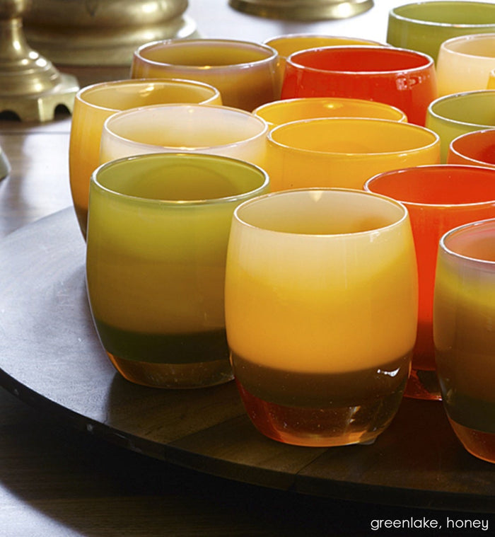 greenlake, olive green hand-blown glass votive candle holder with honey and sweet patootie on a round tray on a table.