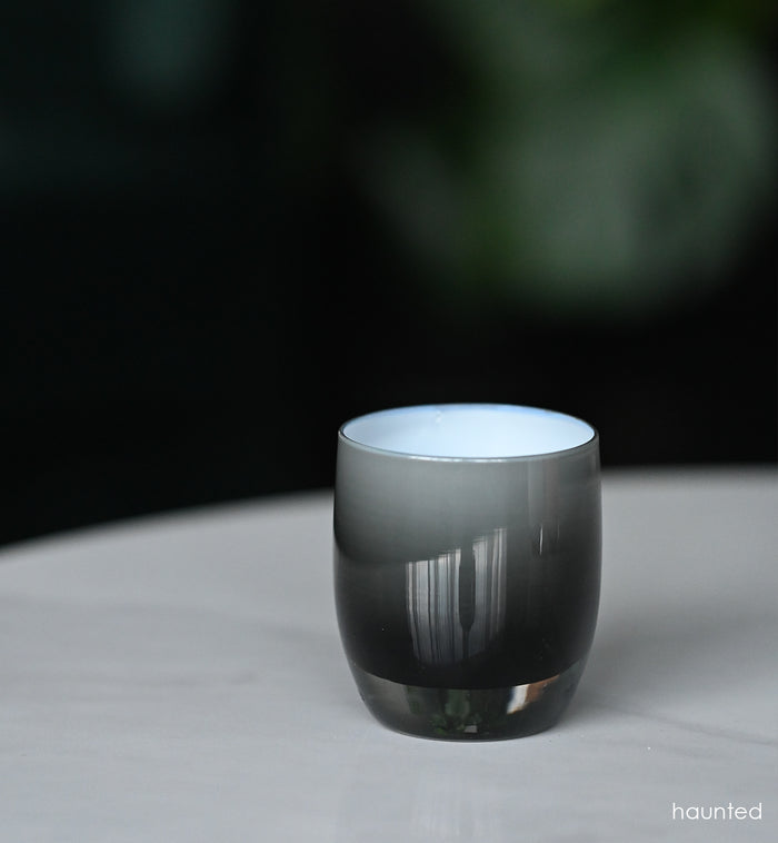 haunted black double overlay hand-blown glass votive candle holder on a marble table outside.