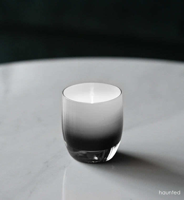 haunted black double overlay hand-blown glass votive candle holder on a marble table, lit with a tealight.