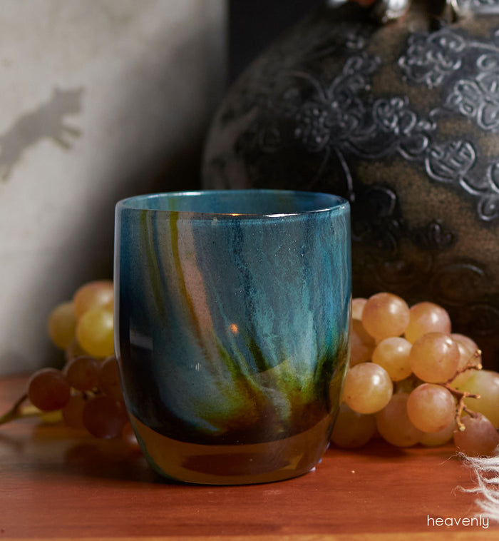 heavenly, blue green swirl, hand-blown glass votive candle holder atop a table with a vase and grapes.