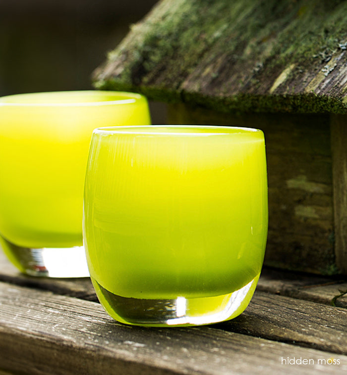 hidden moss, pear green, hand-blown glass votive candle holder next to bowl of steaming contents and mossy birdhouse.