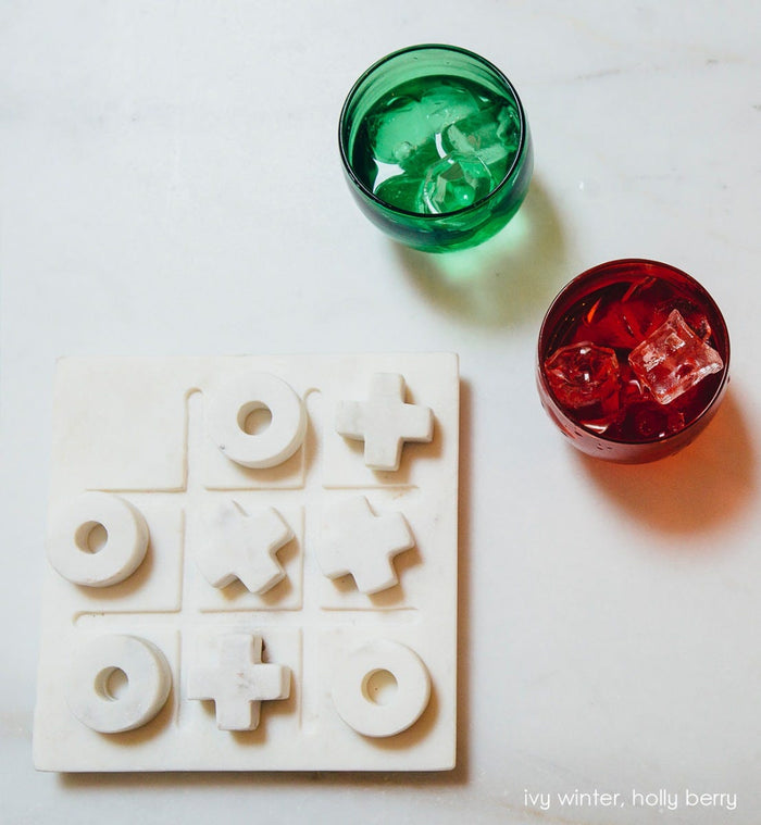 ivy winter drinker transparent green hand-blown drinking glasswith holly berry drinker, both filled with ice and liquid next to a tic tac toe set.