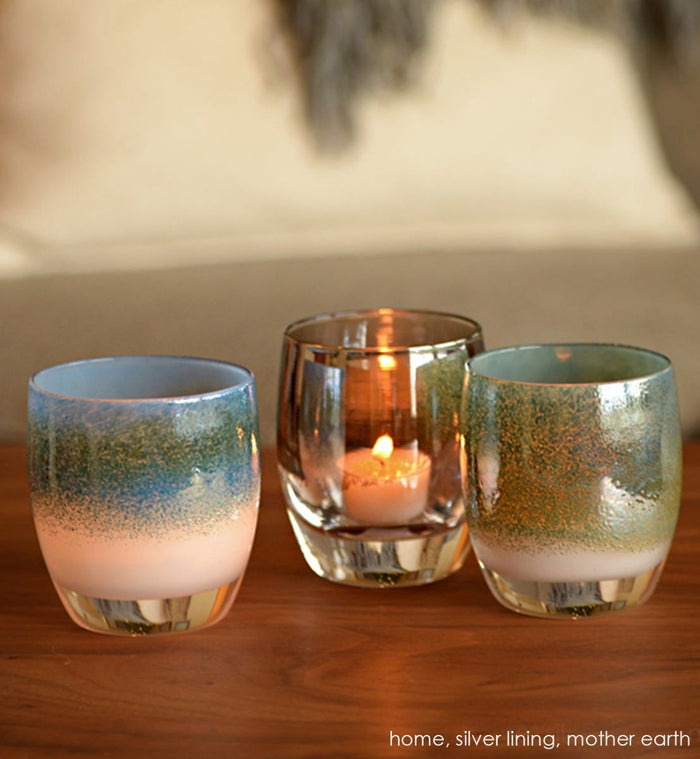 home blue green metallic on white, hand-blown glass votive candle holder. Paired with silver lining and mother earth on a wood table.