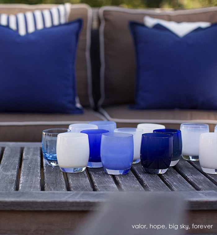 hope pure white hand-blown glass votive candle holder. Paired with valor, big sky, and forever on a wood patio coffee table.