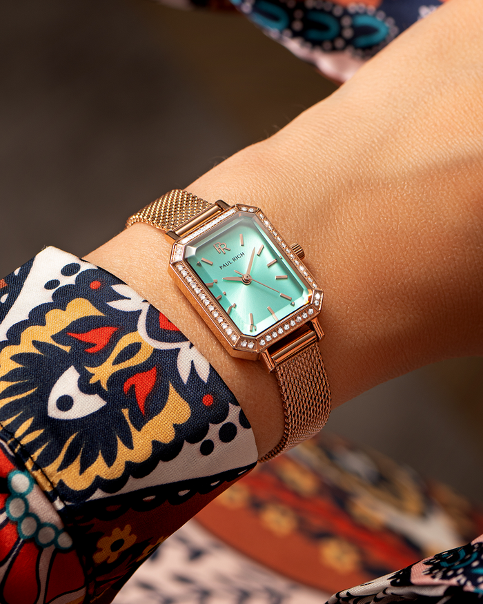 Rose gold Paul Rich watch with a mint green sunray dial, gem-set octagonal bezel, and rose gold mesh strap, worn on wrist with a colorful patterned sleeve.