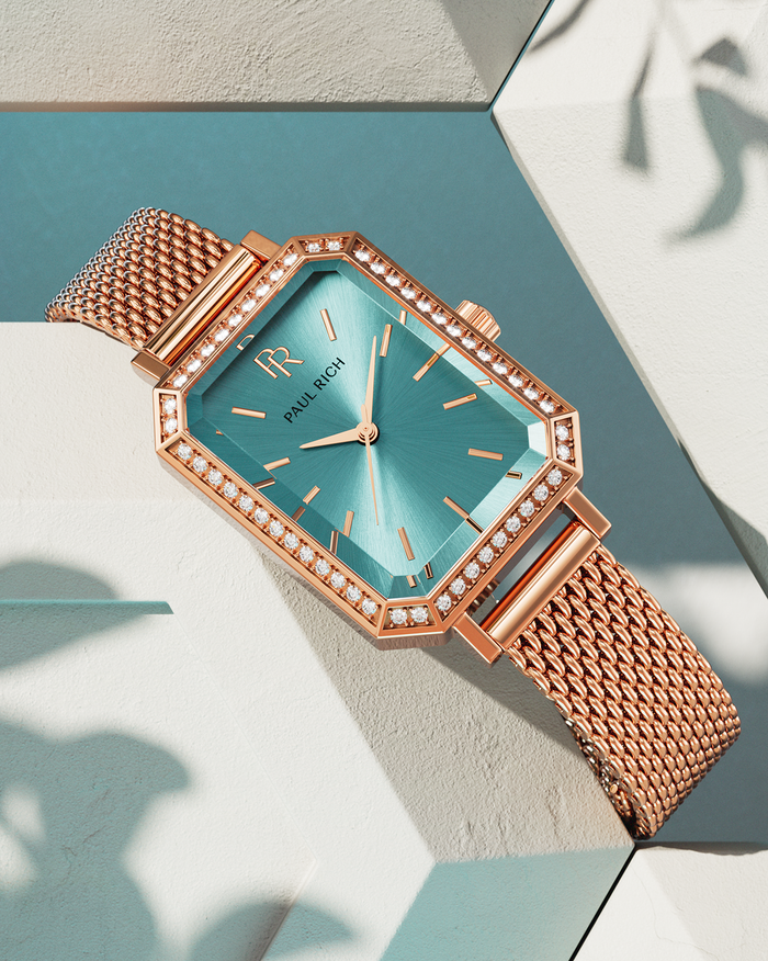 Rose gold Paul Rich watch with a turquoise sunray dial, gem-set octagonal bezel, and rose gold mesh strap, displayed on geometric cream and teal blocks with soft shadows.