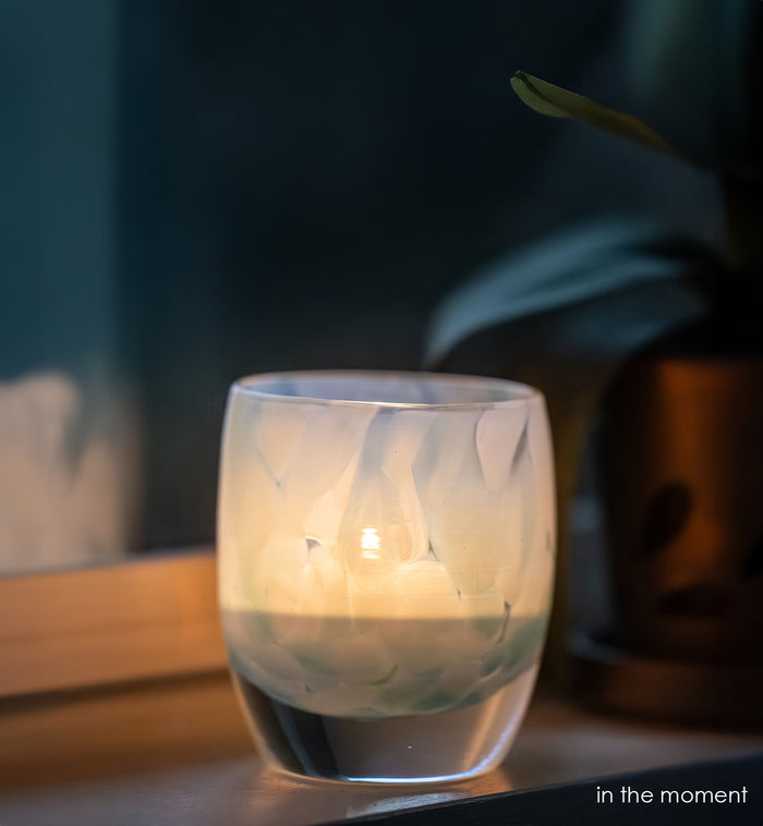 in the moment, blue, white, hand-blown glass votive candle holder with a lit candle on a wooden surface, dark background
